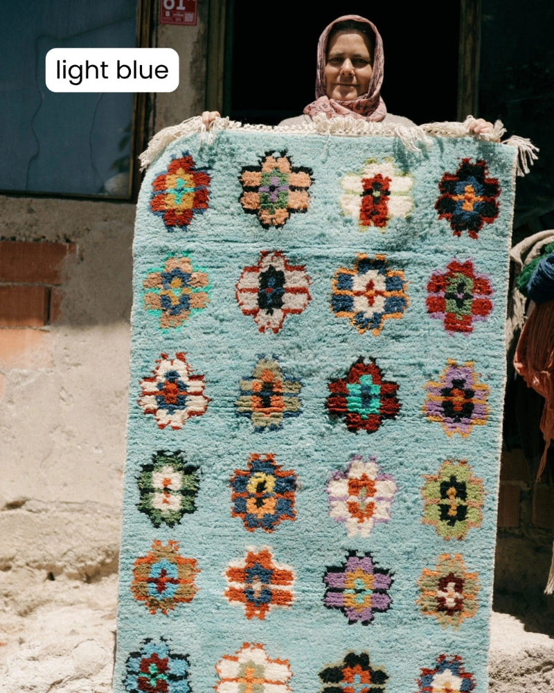 Woman holding a light blue rug with colorful floral patterns.