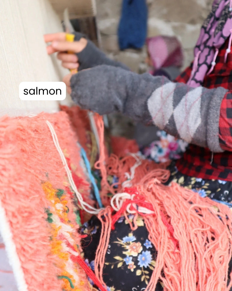 Person holding salmon-colored yarn with a blurred background