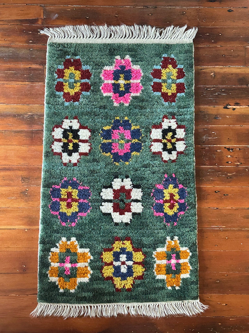 Decorative rug with floral patterns on a wooden floor, featuring a wicker table with decorative items.