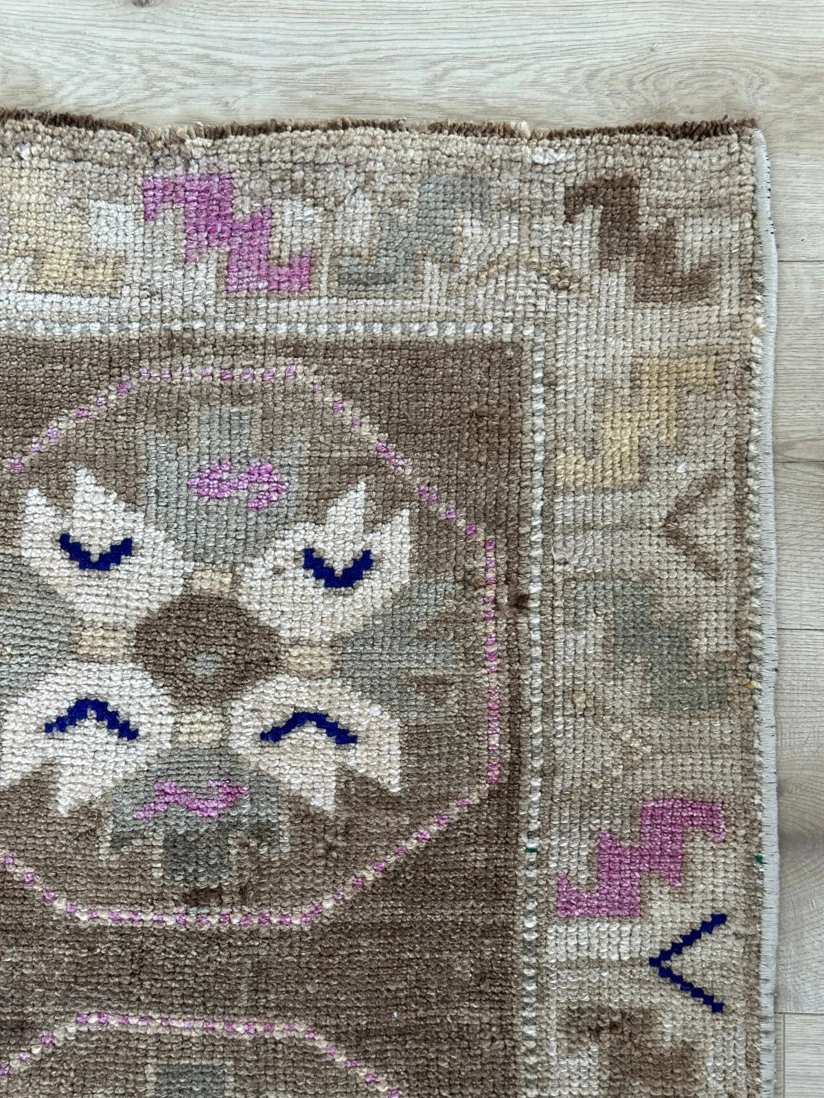 Handmade neutral Turkish mini rug featuring sand, brown and pops of pink and blue with geometric patterns around the border