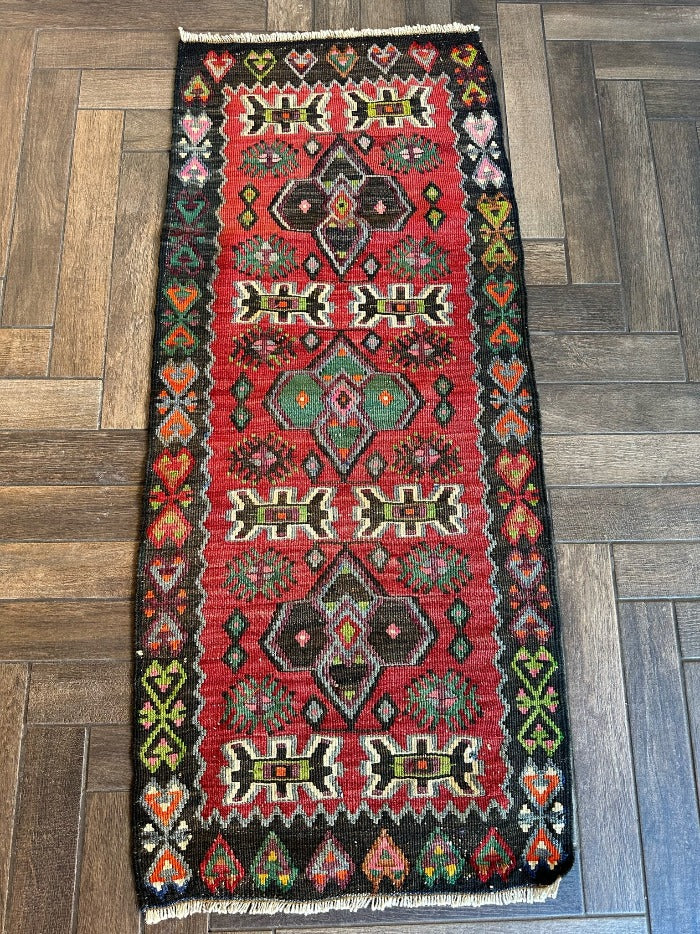 4.5 foot by 2 foot small Turkish kilim runner featuring a black border and geometric patterns throughout in jewel tones