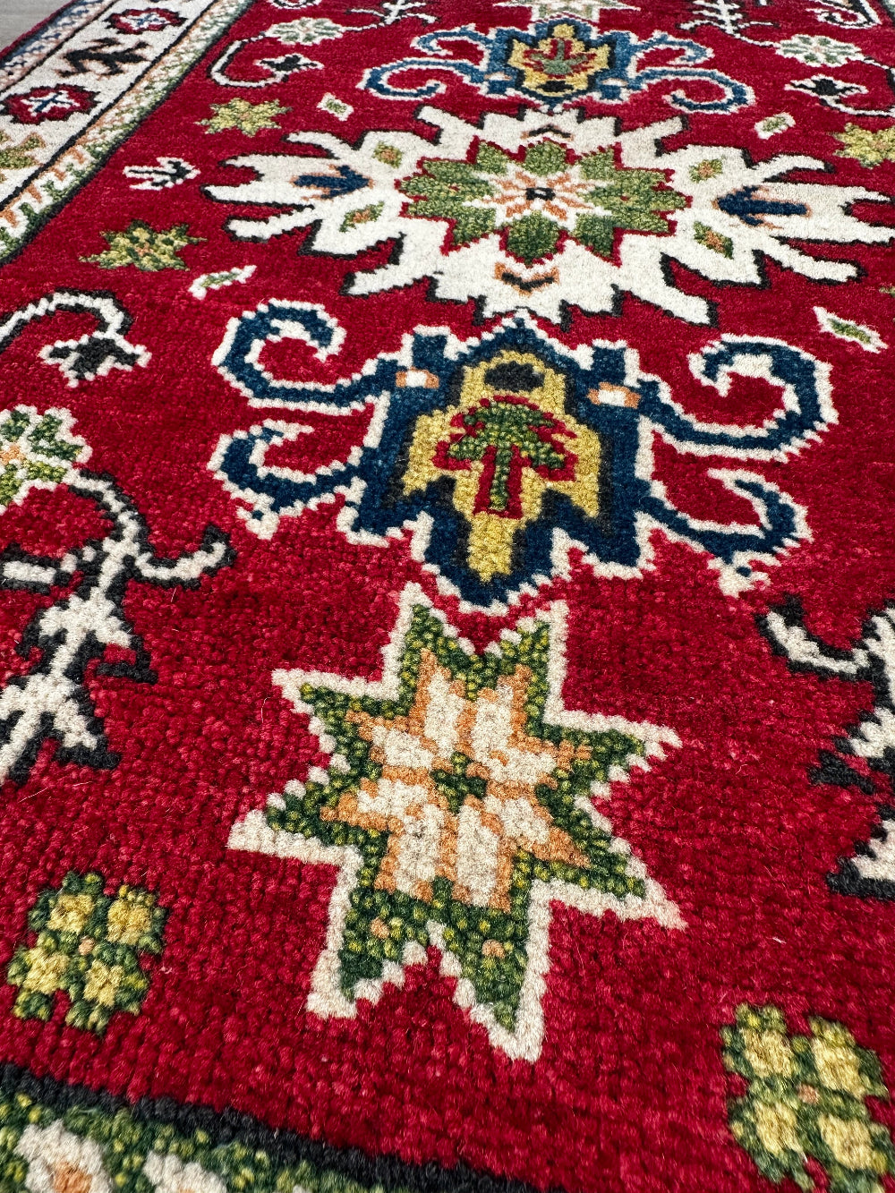 Hand-knotted 2x3 foot mini pile rug featuring a colorful geometric design, large central motif and geometric border - wool material with pops of red, green, navy and white.