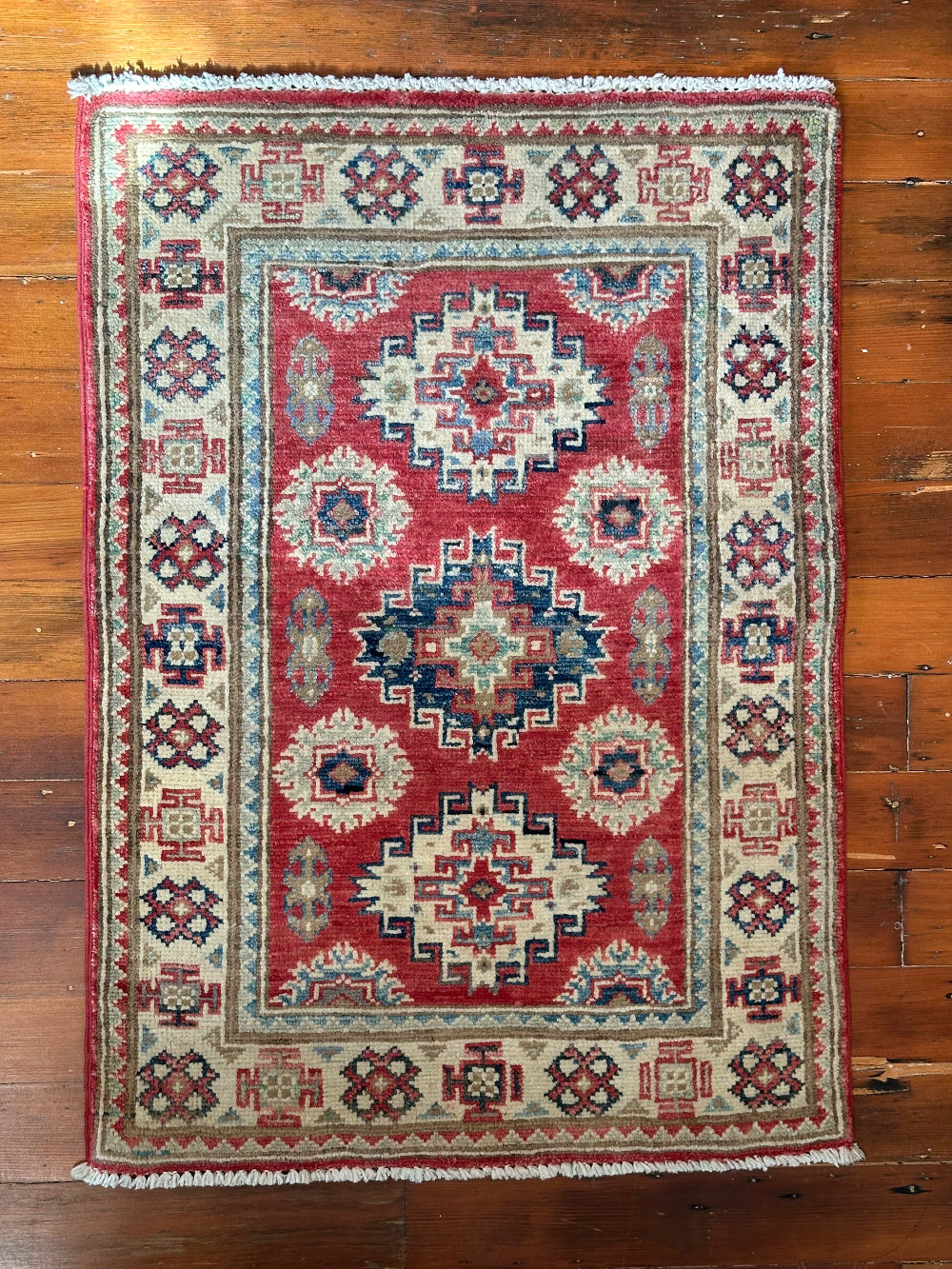 Hand-knotted 2x3 foot mini pile rug featuring a colorful geometric design, large central motif and geometric border - wool material with pops of red, light blue, navy and white.