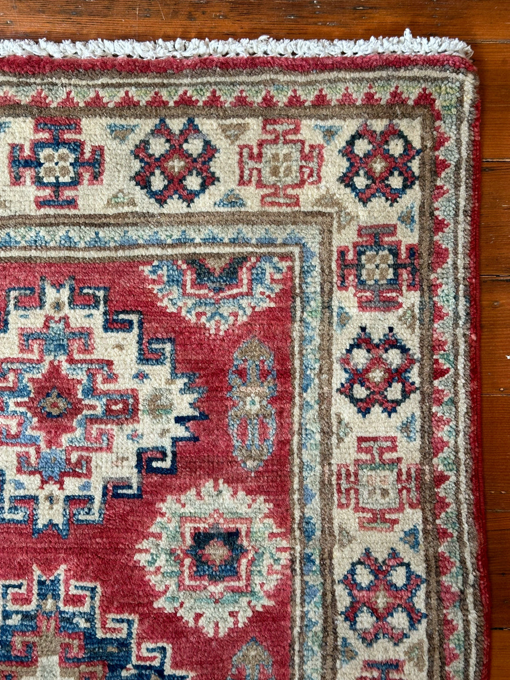Hand-knotted 2x3 foot mini pile rug featuring a colorful geometric design, large central motif and geometric border - wool material with pops of red, light blue, navy and white.