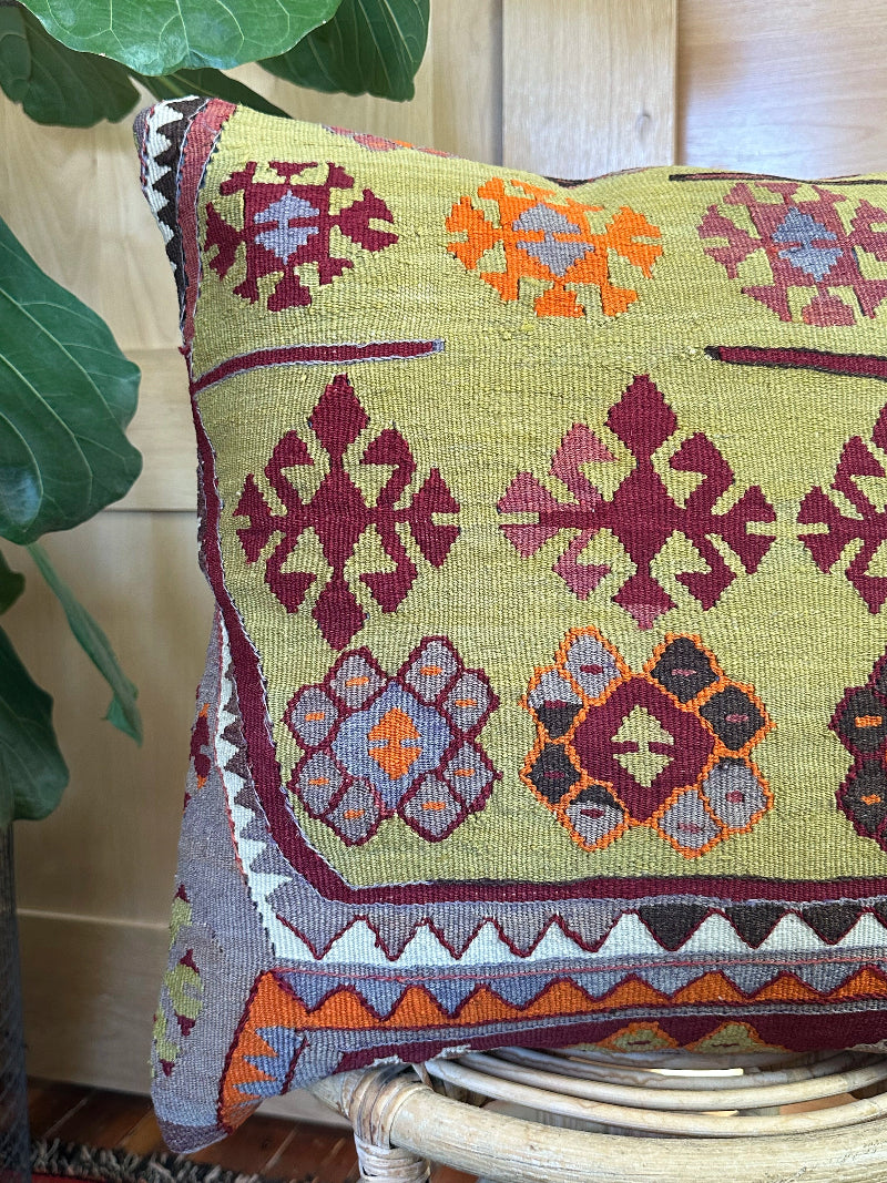 Handwoven kilim pillow crafted from upcycled Turkish rugs, featuring vibrant tribal motifs in olive green, burgundy, orange, and gray tones