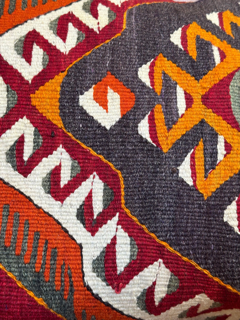 Close-up of a textured fabric with geometric pattern in red, orange, and gray.