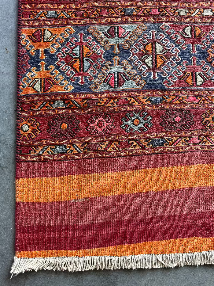 5 by 3 red and orange Turkish area rug featuring a striped pattern on the outside edges and a central striped pattern with geometric shapes and embroidery