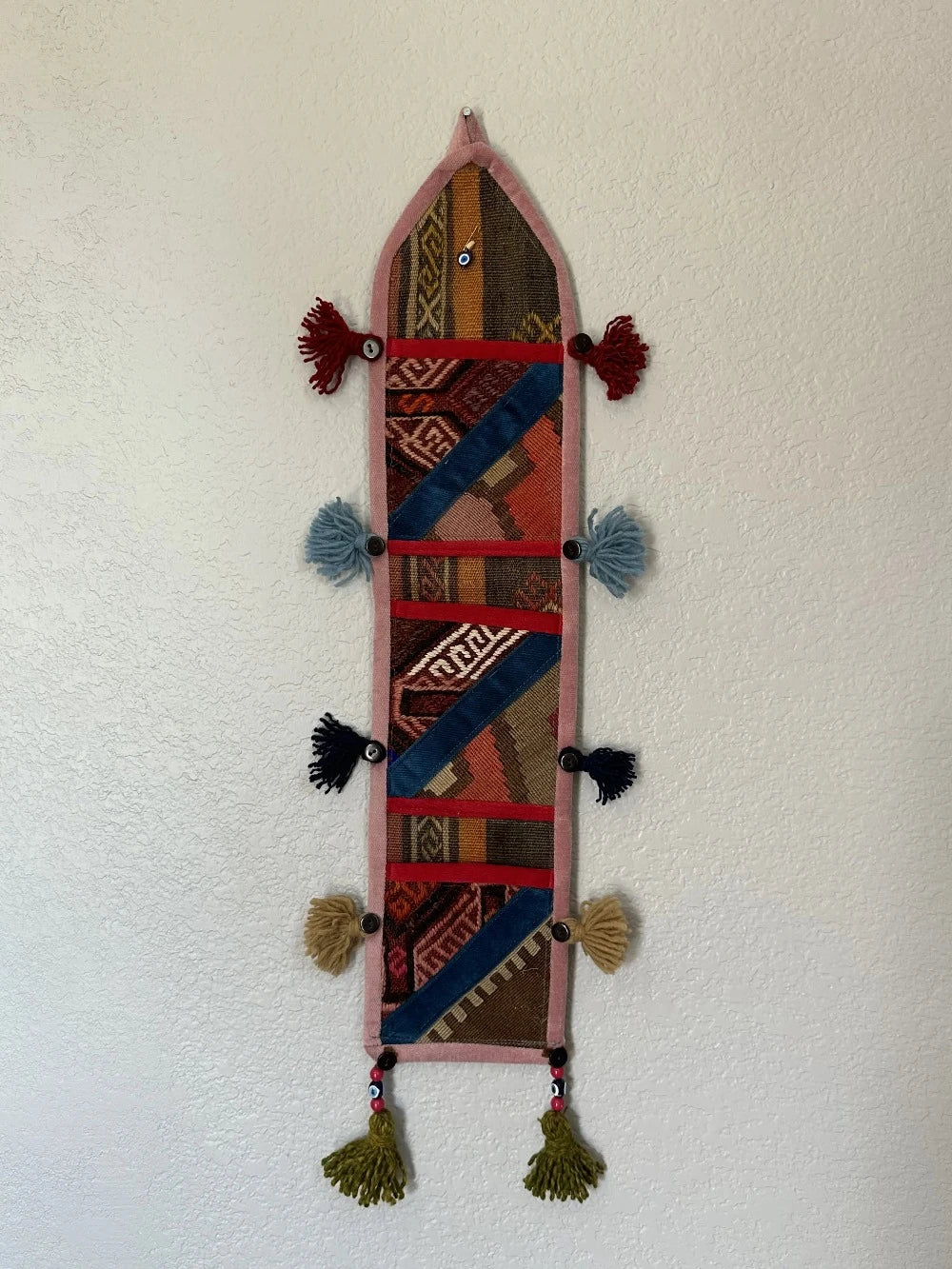 multi-colored three pocket wall organizer made from scraps of colorful Turkish kilim rugs with yarn tassels at each end