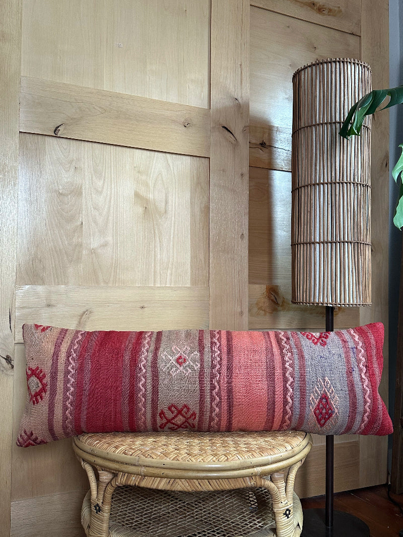 Extra-long vintage Turkish kilim pillow in red, pink, and earthy tones with vertical stripes and traditional geometric motifs, handwoven from wool.