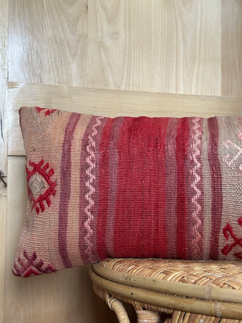 Extra-long vintage Turkish kilim pillow in red, pink, and earthy tones with vertical stripes and traditional geometric motifs, handwoven from wool.