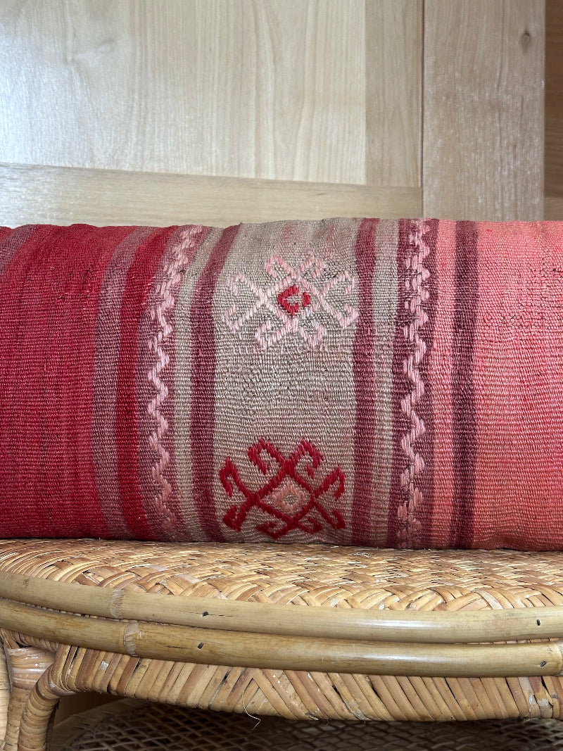 Extra-long vintage Turkish kilim pillow in red, pink, and earthy tones with vertical stripes and traditional geometric motifs, handwoven from wool.