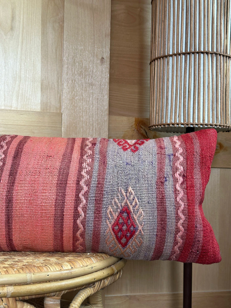 Extra-long vintage Turkish kilim pillow in red, pink, and earthy tones with vertical stripes and traditional geometric motifs, handwoven from wool.