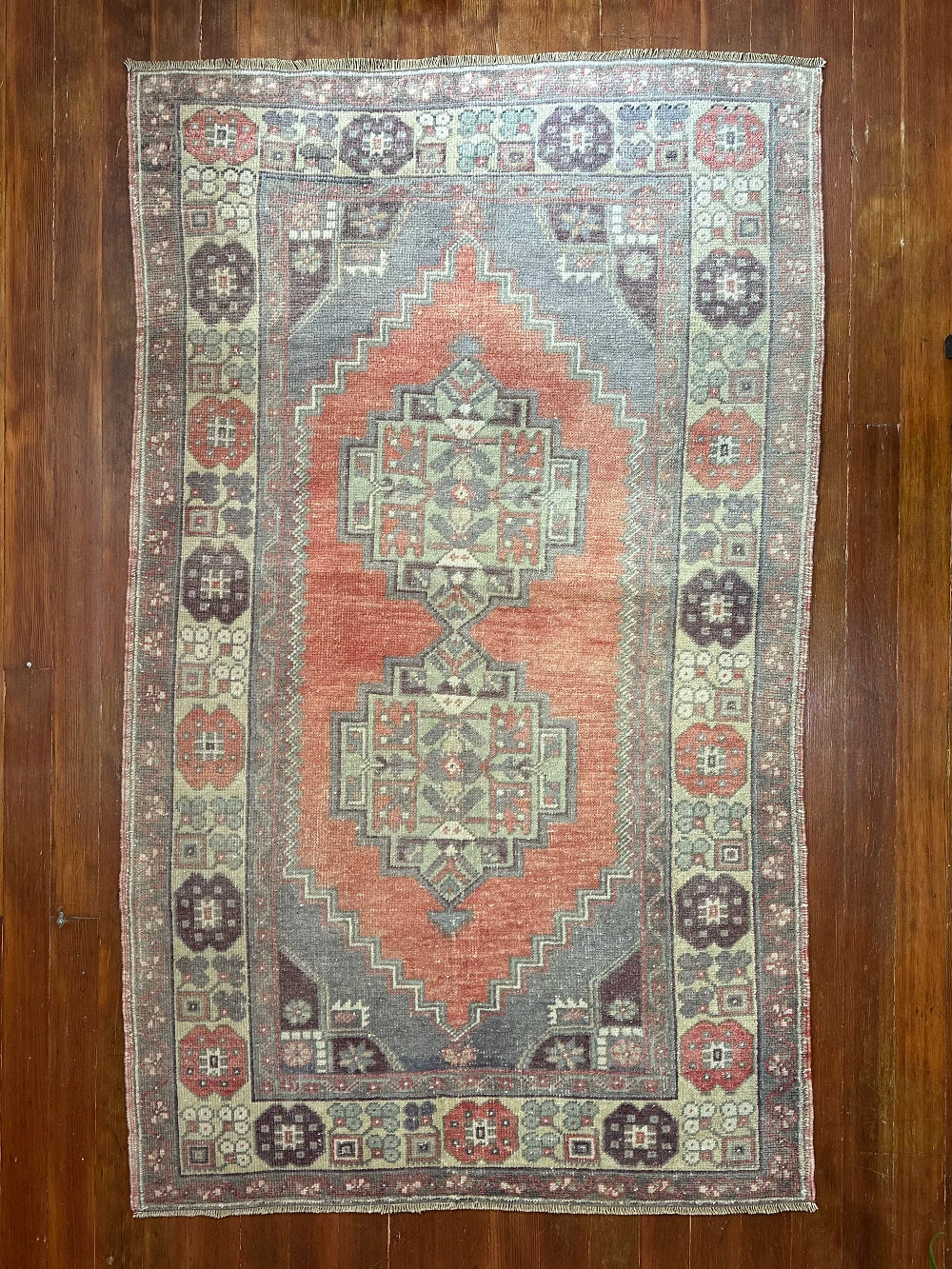 Vintage Turkish handwoven wool rug featuring a double medallion design in muted red, blue, and sage green tones with a detailed floral border.