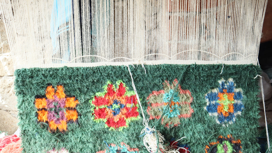 Section of a woven rug with colorful floral patterns on a wooden loom.