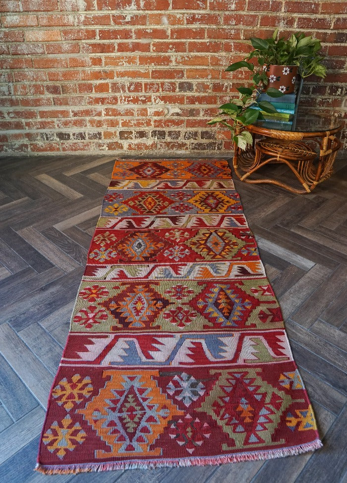 6 by 2.5 small colorful Turkish kilim runner featuring multicolored stripes around 12 inches wide and many different geometric patterns throughout