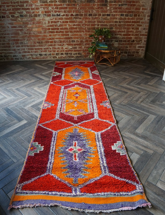 11.5 foot by 3 foot high pile Turkish Herki runner with long shaggy pile and a southwestern feel, orange, red and maroon base coloring and accents of purple, light blue and pink.