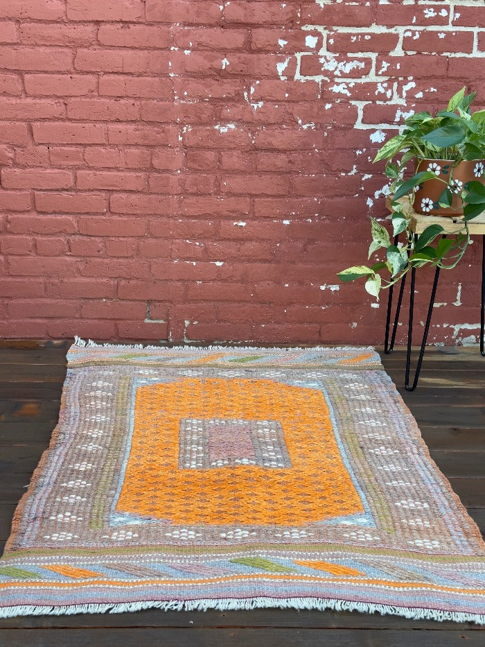 4.5 by 3 colorful turkish area rug featuring bright pops of orange and muted neutrals and pops of blue and green