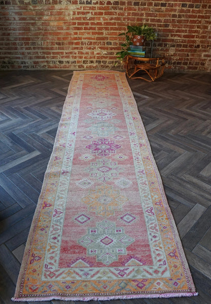 12 feet by 3 ft pink Turkish runner with beautiful large medallions down the center and pops of orange, sand, and dark pink throughout.