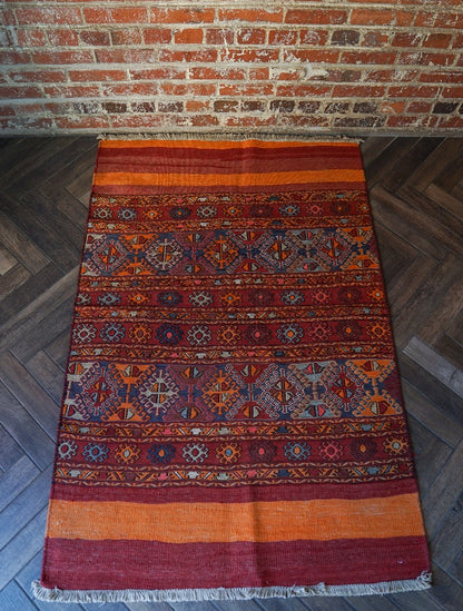 5 by 3 red and orange Turkish area rug featuring a striped pattern on the outside edges and a central striped pattern with geometric shapes and embroidery