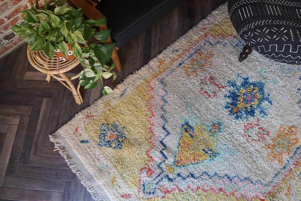 Large high pile Turkish area rug measuring 8 by 5, very muted yellow and cream coloring with pops of blue and orange, perfect for a living room room or bedroom space, unique, one-of-a-kind