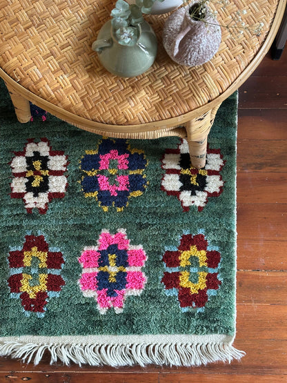 Decorative rug with floral patterns on a wooden floor, featuring a wicker table with decorative items.