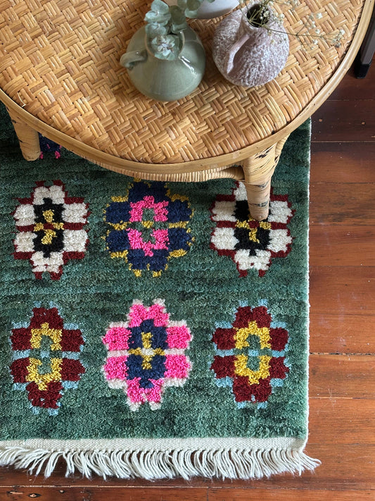 Decorative rug with floral patterns on a wooden floor, featuring a wicker table with decorative items.