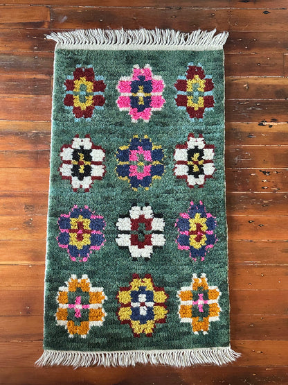 Decorative rug with floral patterns on a wooden floor, featuring a wicker table with decorative items.