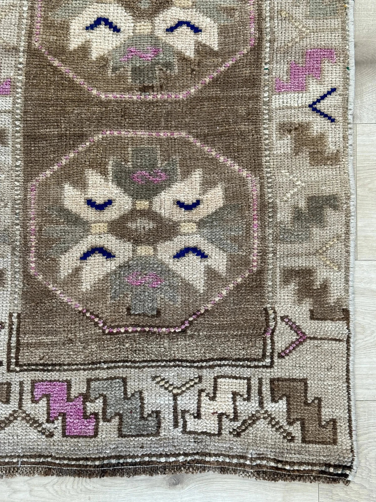 Handmade neutral Turkish mini rug featuring sand, brown and pops of pink and blue with geometric patterns around the border