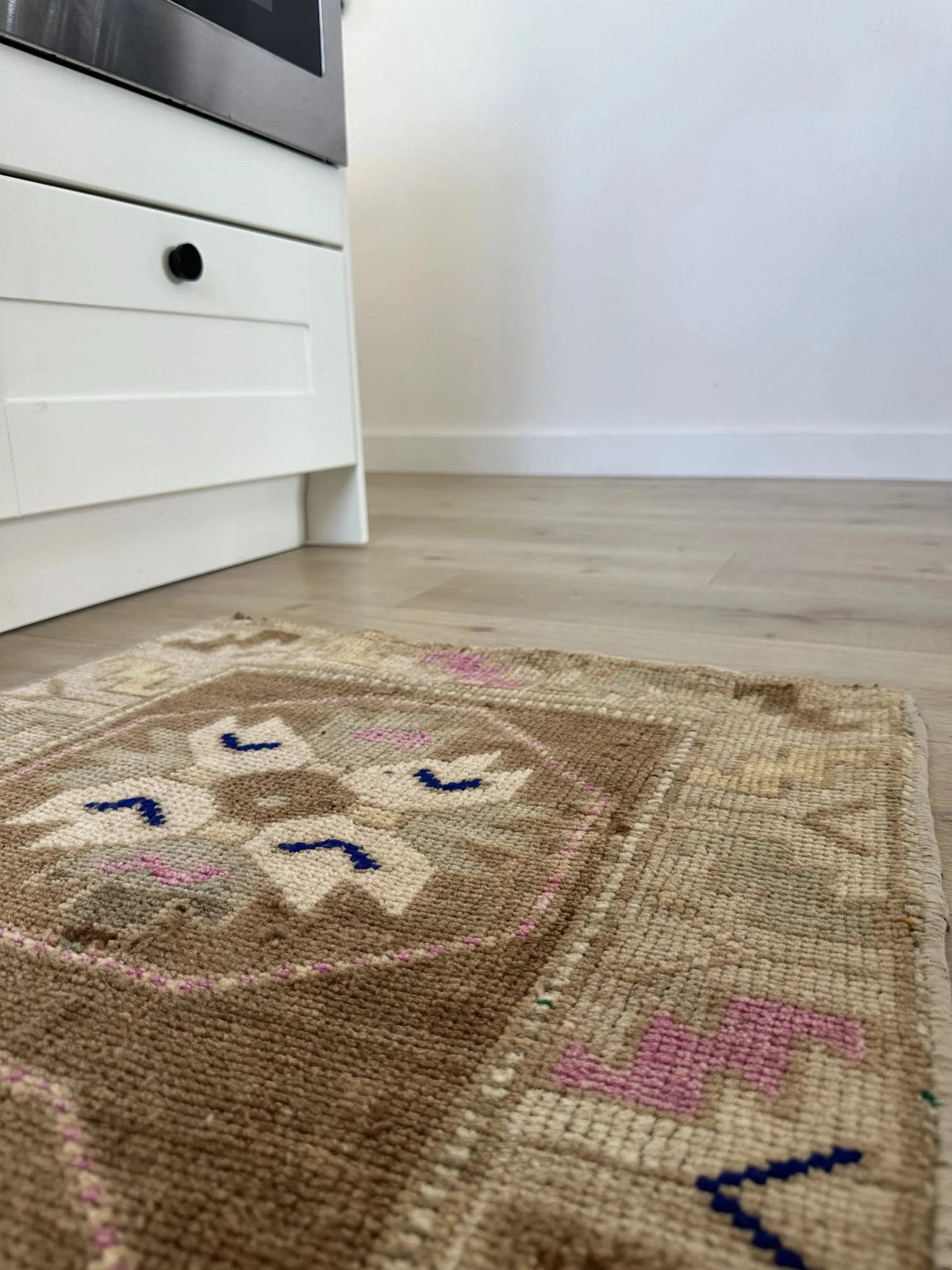 Handmade neutral Turkish mini rug featuring sand, brown and pops of pink and blue with geometric patterns around the border