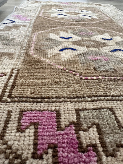 Handmade neutral Turkish mini rug featuring sand, brown and pops of pink and blue with geometric patterns around the border