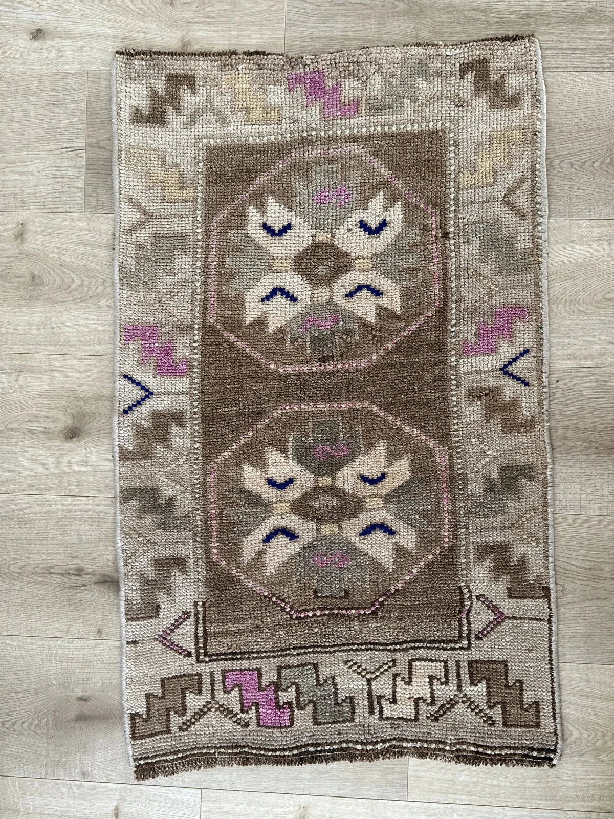 Handmade neutral Turkish mini rug featuring sand, brown and pops of pink and blue with geometric patterns around the border