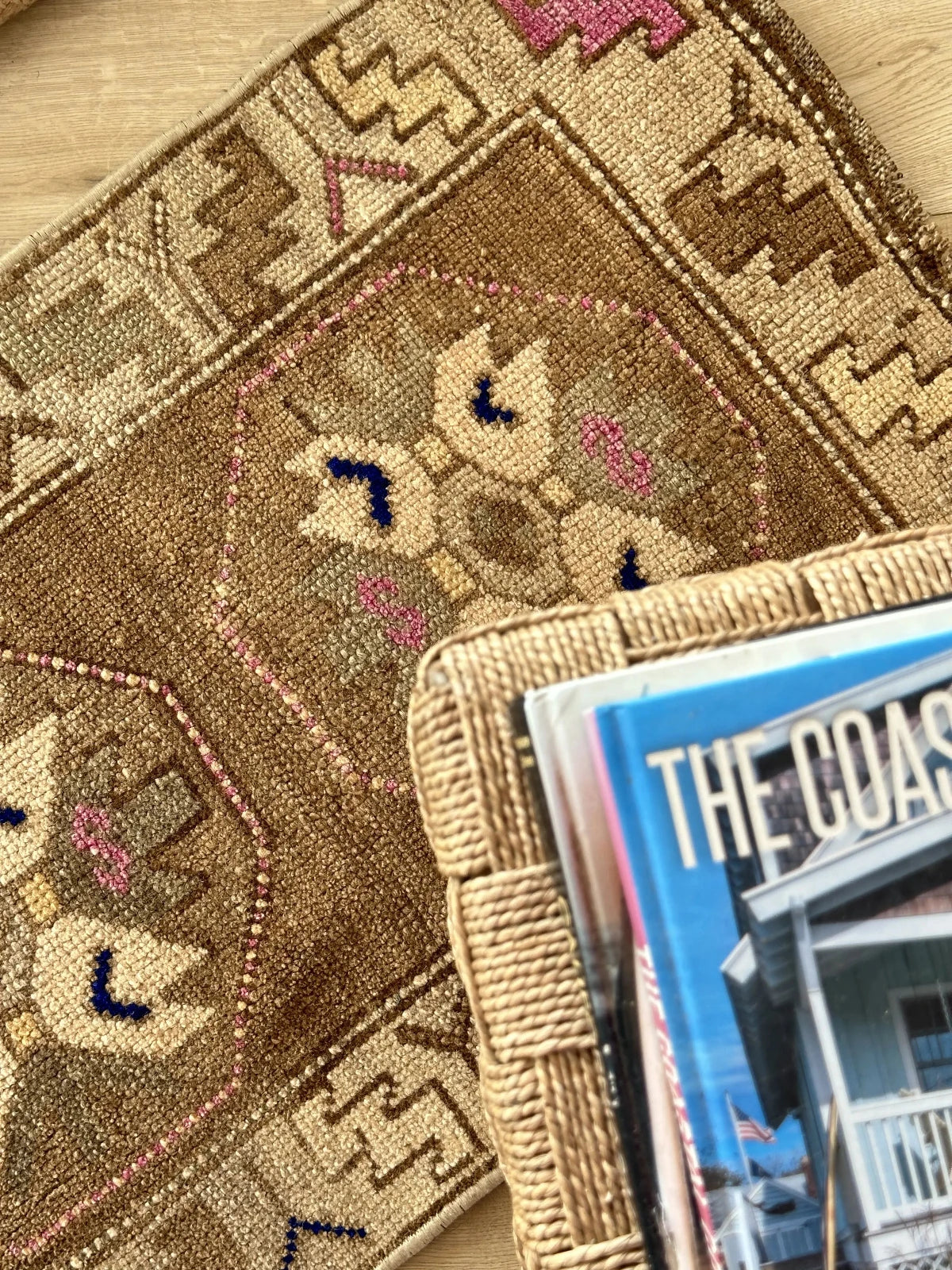 Handmade neutral Turkish mini rug featuring sand, brown and pops of pink and blue with geometric patterns around the border