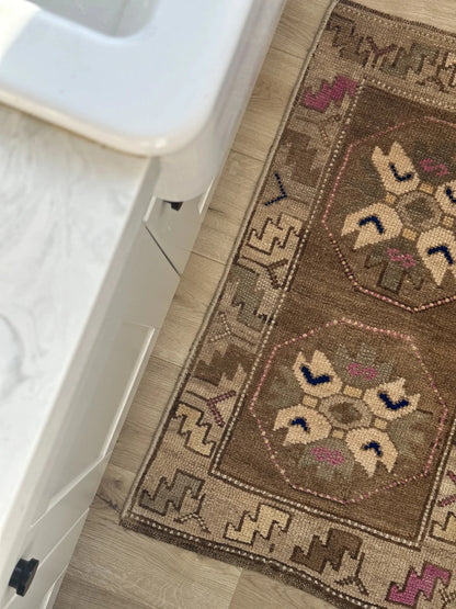 Handmade neutral Turkish mini rug featuring sand, brown and pops of pink and blue with geometric patterns around the border