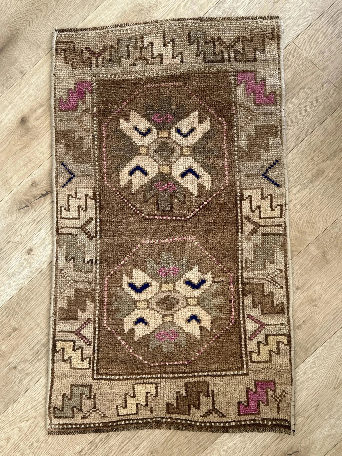 Handmade neutral Turkish mini rug featuring sand, brown and pops of pink and blue with geometric patterns around the border