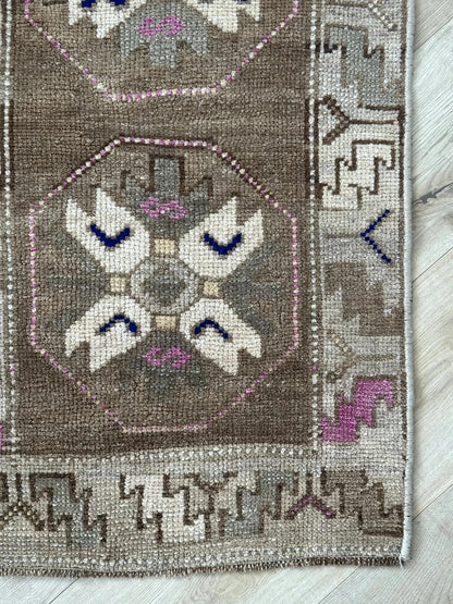 Handmade neutral Turkish mini rug featuring sand, brown and pops of pink and blue with geometric patterns around the border