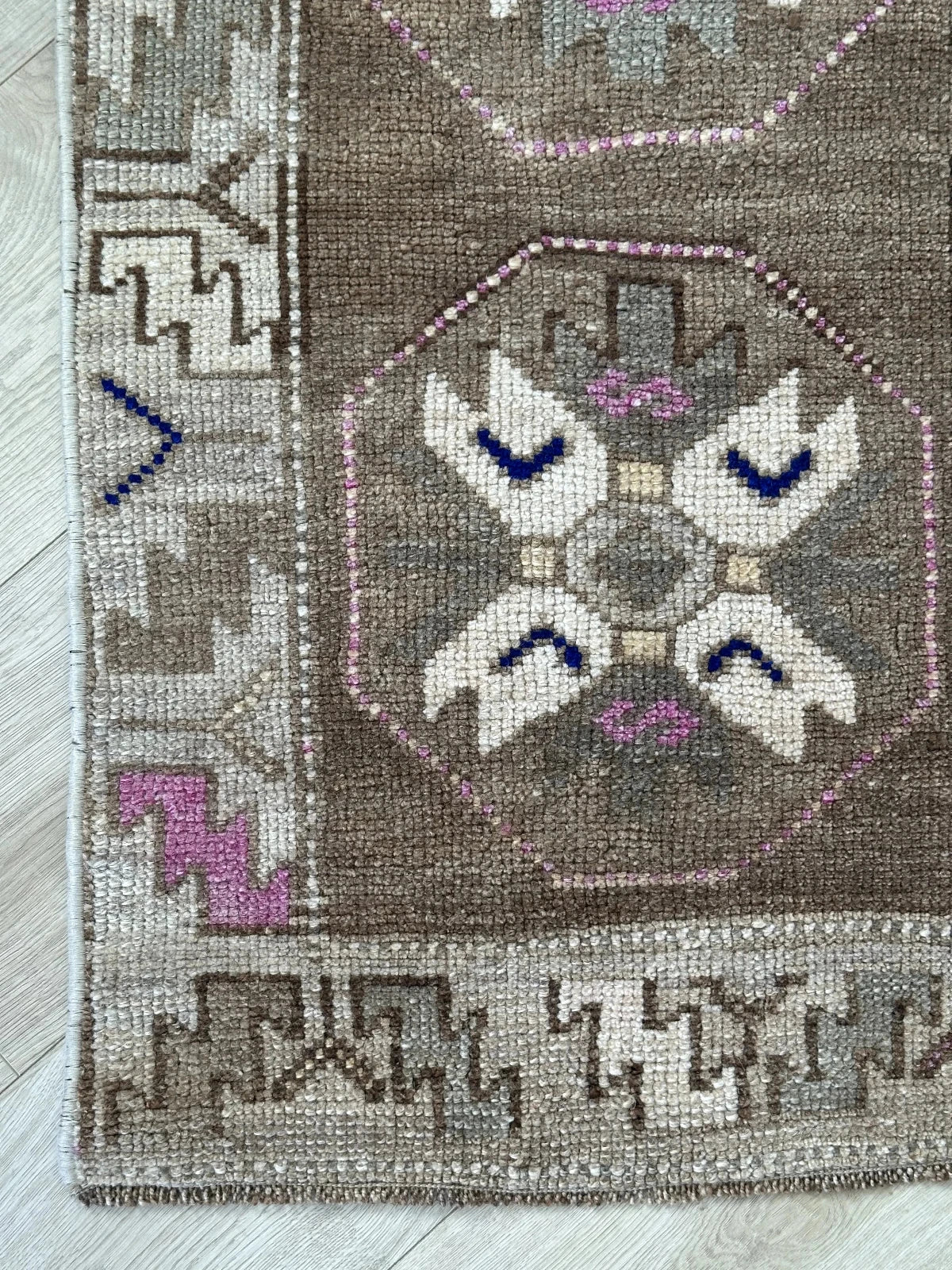 Handmade neutral Turkish mini rug featuring sand, brown and pops of pink and blue with geometric patterns around the border