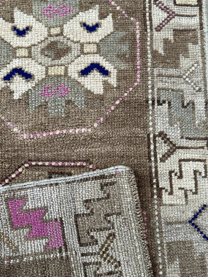 Handmade neutral Turkish mini rug featuring sand, brown and pops of pink and blue with geometric patterns around the border