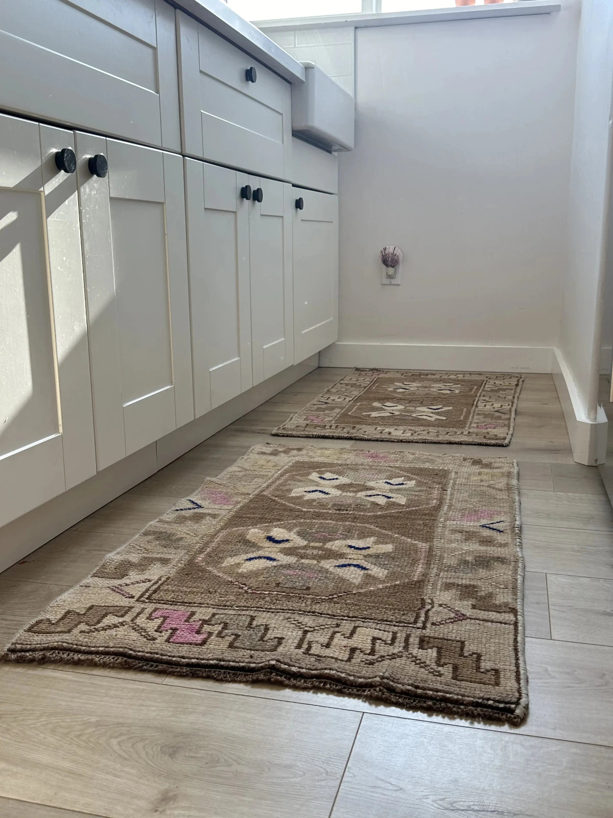 Handmade neutral Turkish mini rug featuring sand, brown and pops of pink and blue with geometric patterns around the border