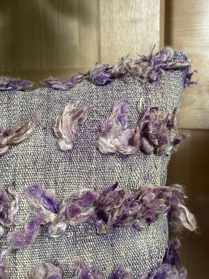 16 by 16 Turkish pillow featuring a neutral-toned woven base with soft, curly wool tufts in shades of purple and lavender, creating a unique, organic pattern. The intricate details and rich texture highlight the craftsmanship and artisanal nature of the piece