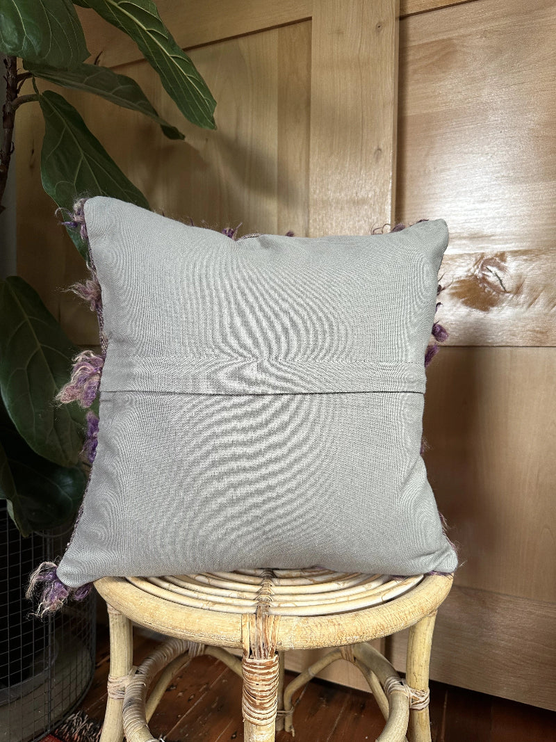 16 by 16 Turkish pillow featuring a neutral-toned woven base with soft, curly wool tufts in shades of purple and lavender, creating a unique, organic pattern. The intricate details and rich texture highlight the craftsmanship and artisanal nature of the piece