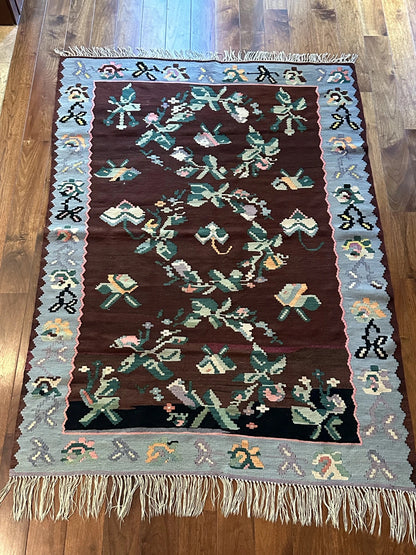 Large handmade rug featuring a sky blue floral border and a coffee brown inner field with large floral design