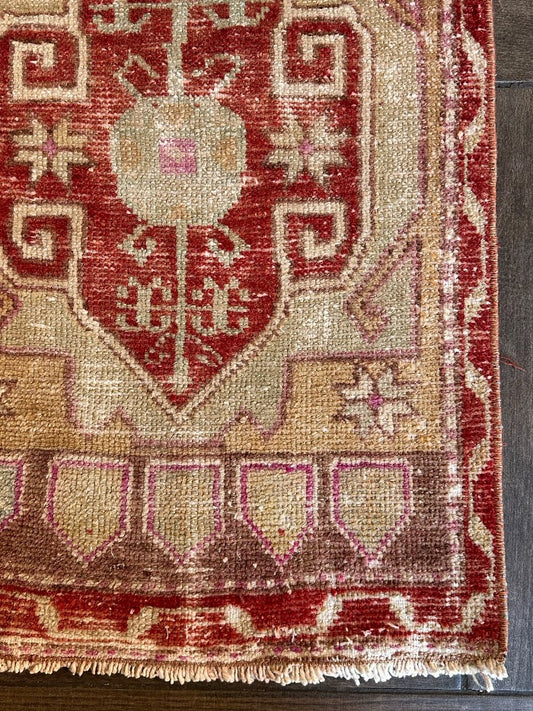 4 by 2 small Turkish area rug featuring deep red hues and light sand and tan coloring with two large medallions in the center bordered by geometric shapes and florals