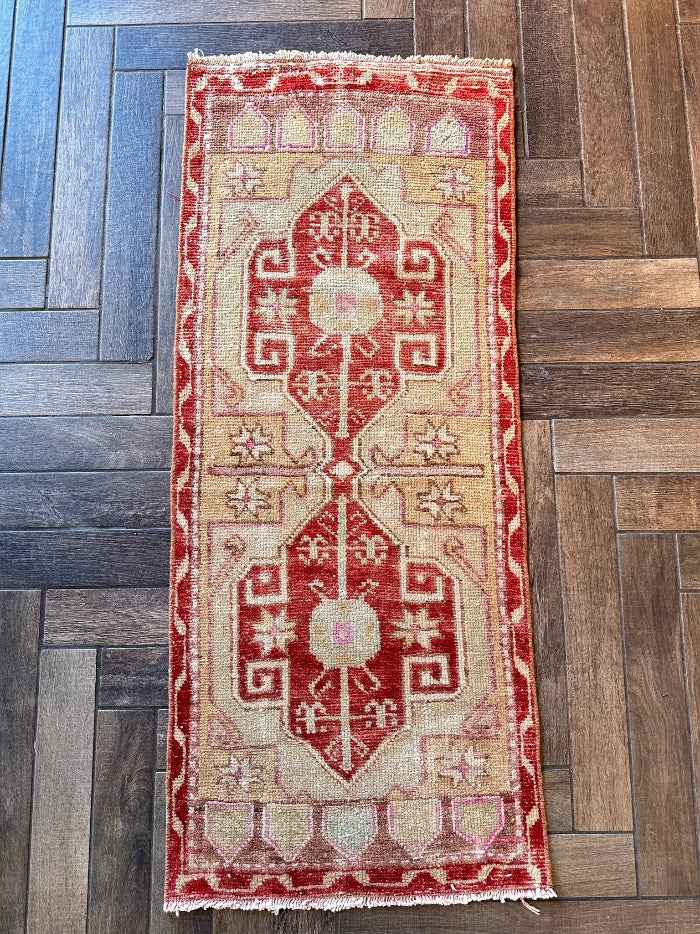 4 by 2 small Turkish area rug featuring deep red hues and light sand and tan coloring with two large medallions in the center bordered by geometric shapes and florals