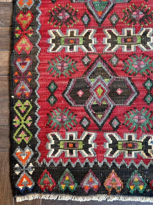 4.5 foot by 2 foot small Turkish kilim runner featuring a black border and geometric patterns throughout in jewel tones