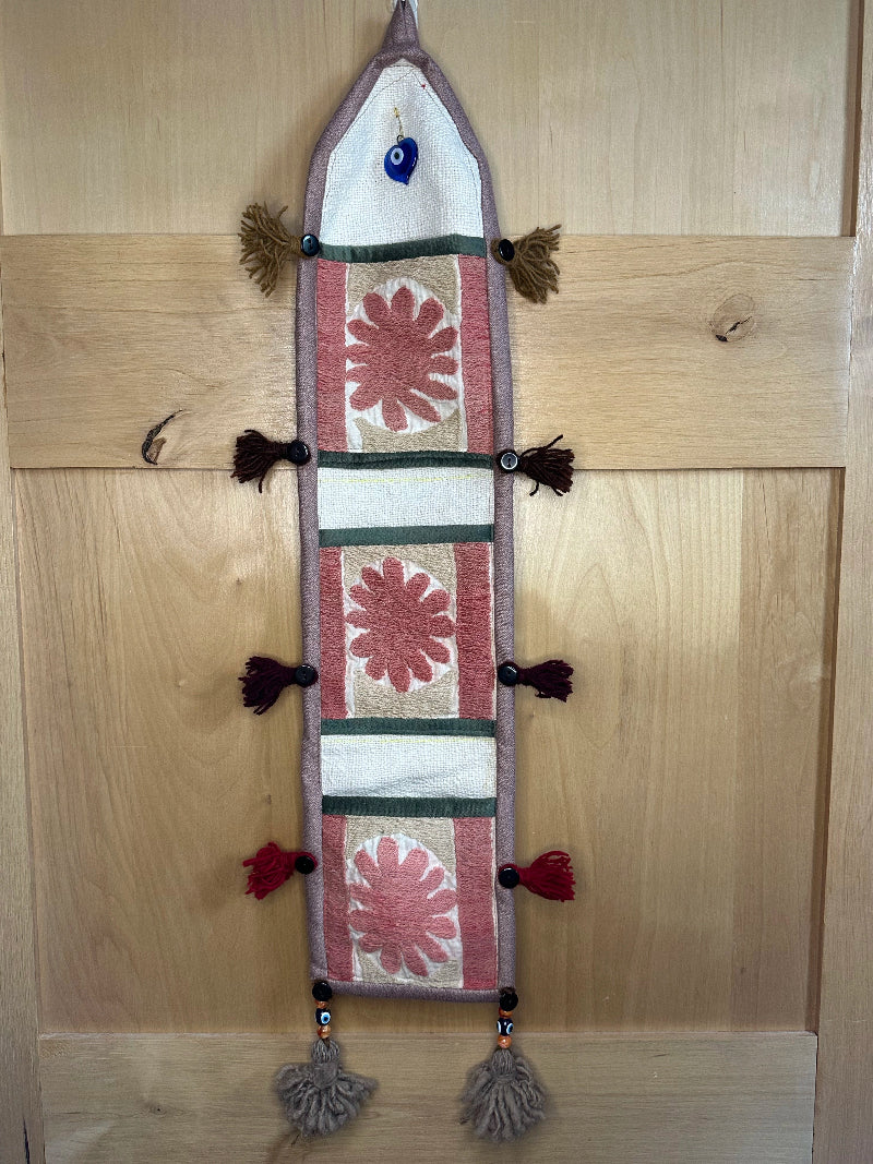 Handmade Turkish rug wall hanging with pink floral designs, tassels, and an evil eye charm. Upcycled vintage textile art by High Pile Designs.