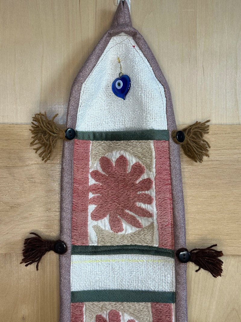 Handmade Turkish rug wall hanging with pink floral designs, tassels, and an evil eye charm. Upcycled vintage textile art by High Pile Designs.