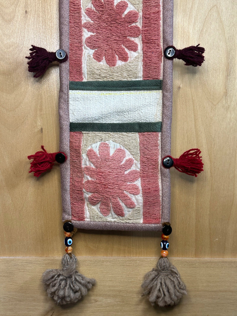 Handmade Turkish rug wall hanging with pink floral designs, 3 pockets, tassels, and evil eye charm. Upcycled vintage textile art by High Pile Designs.