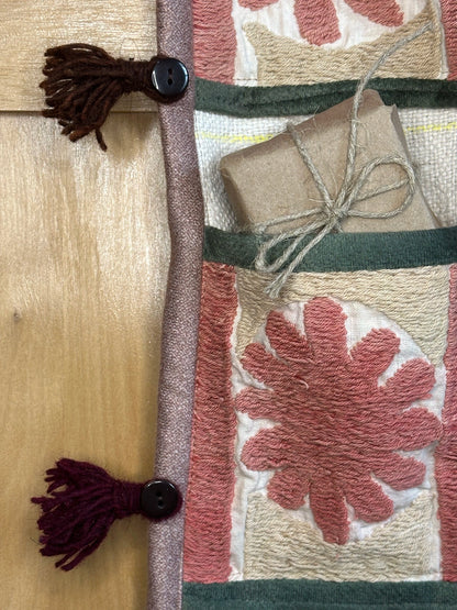 Handmade Turkish rug wall hanging with pink floral designs, 3 pockets, tassels, and evil eye charm. Upcycled vintage textile art by High Pile Designs. Featuring a gift.