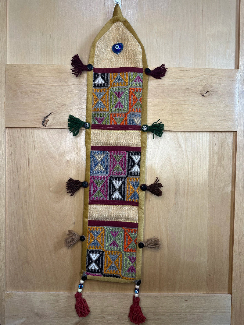 Handmade Turkish rug wall hanging with geometric designs, 3 pockets, tassels, and an evil eye charm. Upcycled vintage textile art by High Pile Designs.