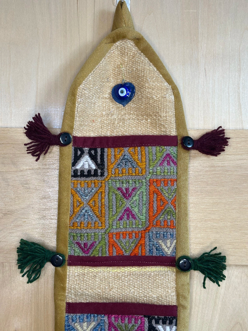 Handmade Turkish rug wall hanging with geometric designs, 3 pockets, tassels, and an evil eye charm. Upcycled vintage textile art by High Pile Designs.